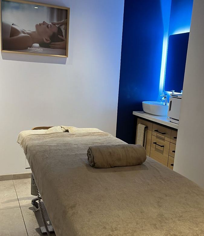 Treatment room with a massage bed, folded towel and a washbasin