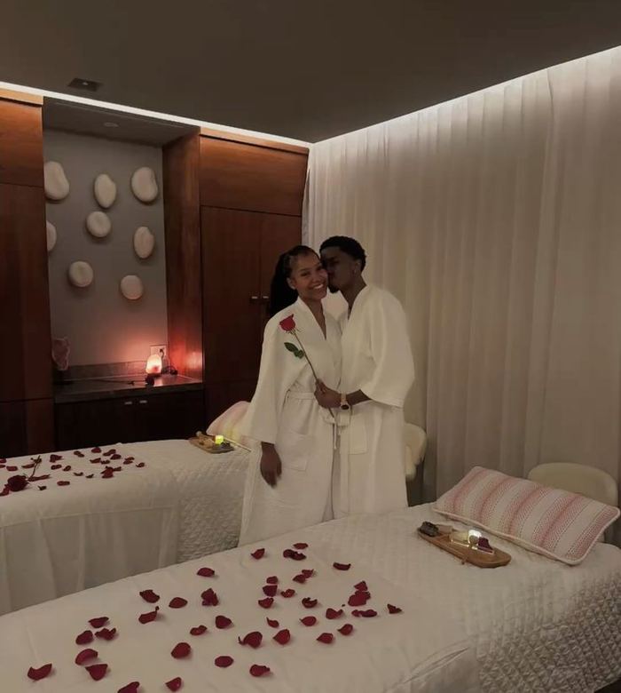 Couple in robes beside two massage beds prepared with rose petals