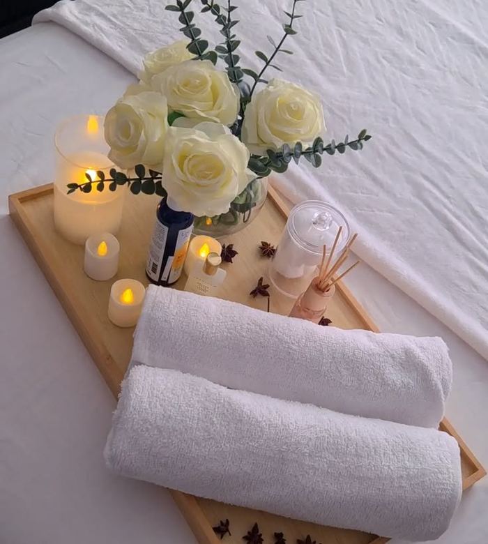 Fresh rolled towels, candles and flowers laid out on a massage bed